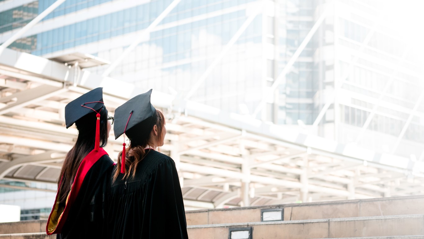 two-girls-black-gowns-standing-look-up-sky-with-happy-graduates.jpg